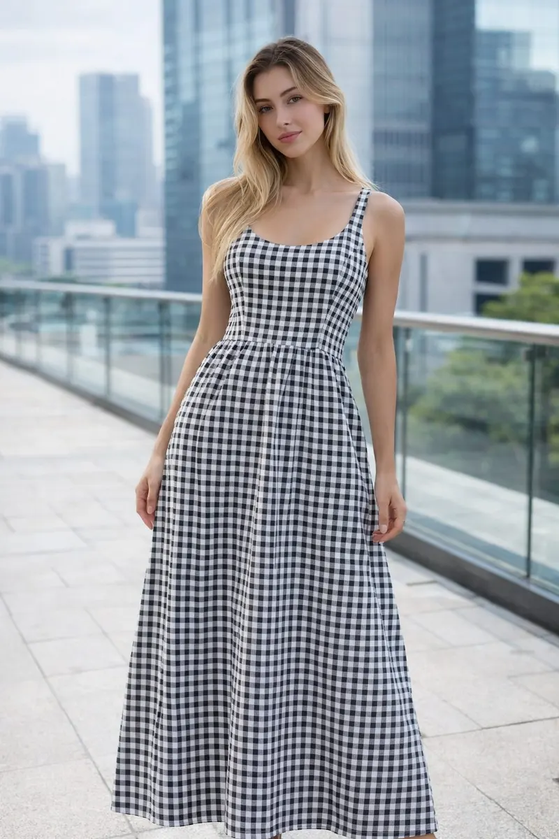 Woman wearing a black and white gingham sleeveless maxi dress in a modern rooftop setting with a soft editorial pose