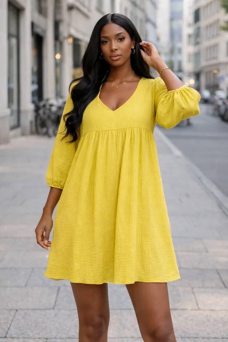 Woman wearing a bright yellow loose-fit mini dress with a V-neckline and voluminous sleeves, styled with minimal jewelry on a softly blurred city street.