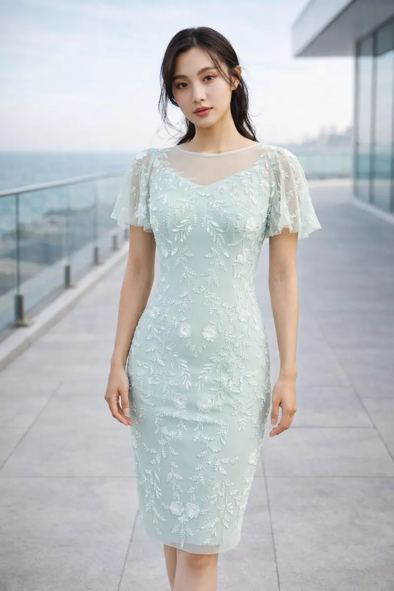 Woman wearing a mint green embroidered fitted midi dress with sheer flutter sleeves in a modern coastal editorial setting