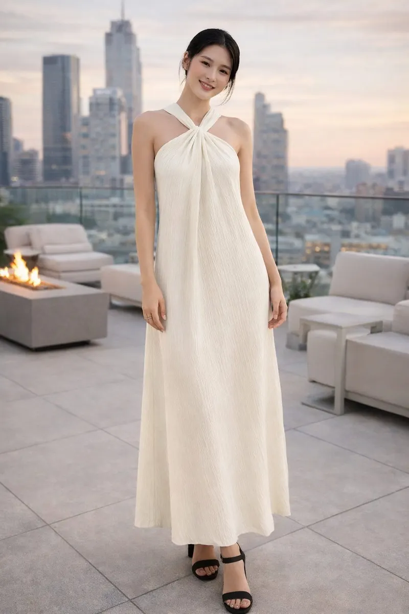 Woman wearing an ivory halter maxi dress with a draped neckline on a modern rooftop terrace at sunset