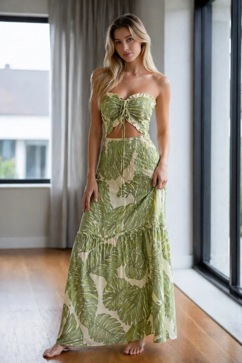 Model wearing a green tropical print strapless maxi dress with cutout waist detail in a polished summer editorial setting