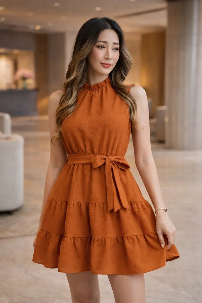 Woman wearing a terracotta sleeveless tiered mini dress with a waist tie in an elegant softly blurred interior setting