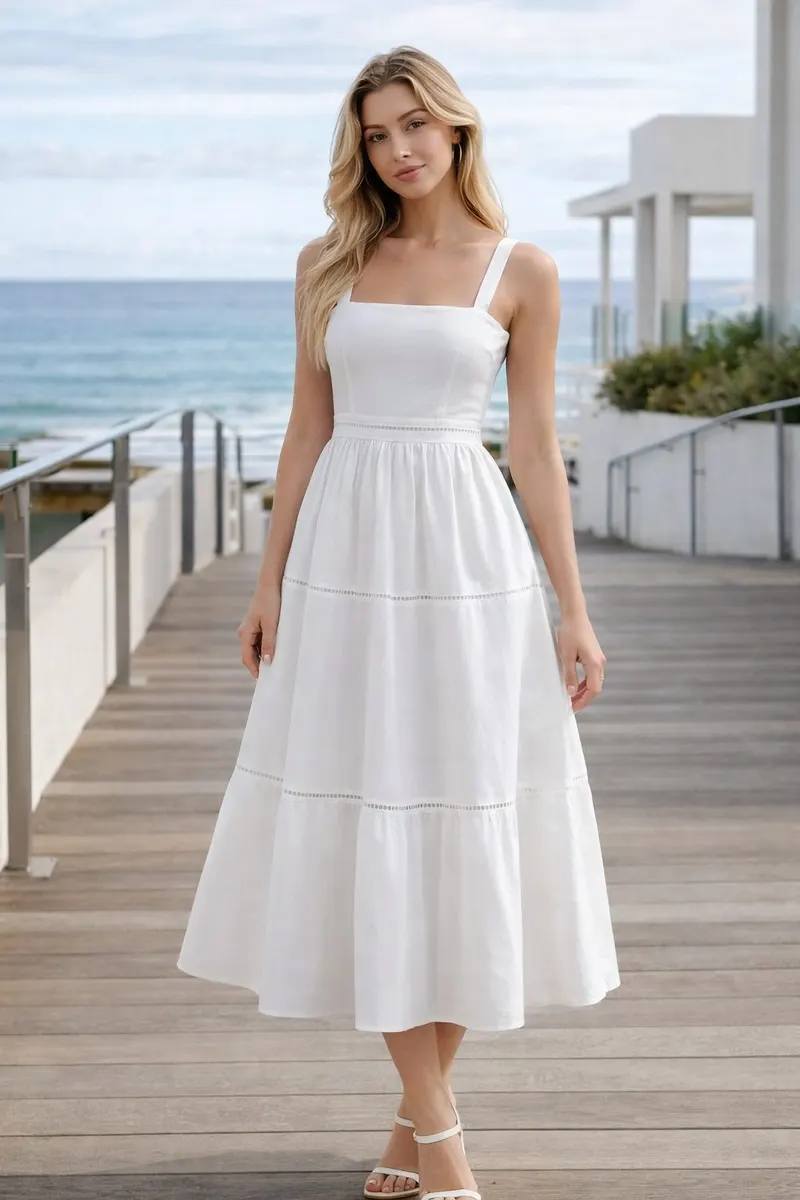Woman wearing a white square-neck midi dress with a softly gathered skirt on a modern coastal walkway